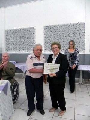 A Presidente do Conselho Municipal do Idoso, senhora Maria Dinora de Moura, entregando o certificado ao senhor Felisbino Franco de Oliveira